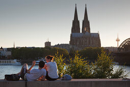 Young couple sitting on the Rhine river banks opposite to the cathedral, Cologne, North Rhine-Westphalia, Germany, Europe