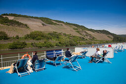 Menschen sonnen sich auf dem Deck von Flusskreuzfahrtschiff MS Bellevue mit Blick auf Weinberge, Rheinland-Pfalz, Deutschland, Europa