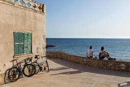 Zwei Rennradfahrer sitzen auf einer Mauer am Mittelmeer, Sant Elm, Mallorca, Balearische Inseln, Spanien