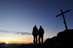 Young woman and young man enjoying sunset at summit of Risserkogel, Bavarian Prealps, Mangfall Mountains, Bavaria, Germany