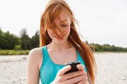 Young woman with a mobile phone at Isar river, Munich, Bavaria, Germany