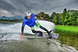 Young man surfing on a wakeboard, wakeboarding at lake Neubeurer See, Neubeuern, Rosenheim, Upper Bavaria, Bavaria, Germany