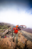 Men carrying mountain bikes over a ridge, Tenerife