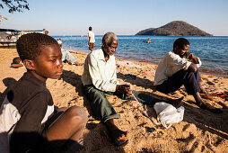 A boy, an old man and a young man sitting on the beach of Lake Malawi and repairing fishing nets, Chembe Village, Cape Mclear, Malawi, Africa
