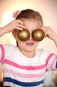 Girl (4 years) covering eyes with two christmas tree balls