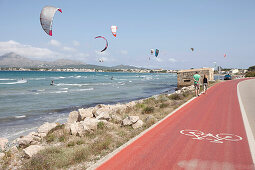 Tourists walking along a bike lane next to the coastal road, kite surfers near Club Pollentia, Badia de Pollenca near Alcudia, Mallorca, Balearic Islands, Spain