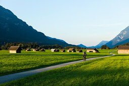 Mountain biker passing meadow with hay barns, Grainau, Bavaria, Germany