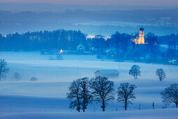 Blick auf winterliches Holzhausen mit Pfarrkirche St. Johann Baptist in der Abenddämmerung, Holzhausen, Münsing, Bayern, Deutschland