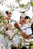 Young woman and fruit farmer between flowering apple trees, Riegersburg, Styria, Austria