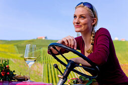Junge Frau sitzt mit einem Glas Weißwein auf einem Traktor, Steiermark, Österreich
