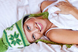 Junge Frau mit Mütze liegt in einem Bett, Steiermark, Österreich