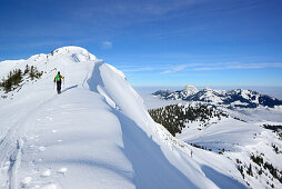 Frau auf Skitour steigt über Grat zu Großer Traithen auf, Wendelstein im Hintergrund, Mangfallgebirge, Bayerische Alpen, Oberbayern, Bayern, Deutschland