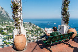 Mann sitzt auf einer Bank und liest Zeitung, Piazzetta, Capri, Kampanien, Italien