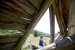 Two female hikers resting near the remains of a wooden lodge, Nockberge, Carinthia, Austria