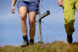 Two female hikers walking the Alpe-Adria-Trail, summit cross in the background, Nockberge, Carinthia, Austria