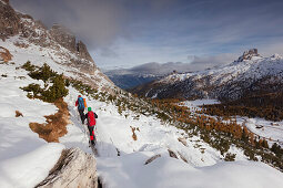 Young couple with backpacks hiking in snow, Fanes-Sennes-Prags Nature Park, valley of the Passo di Falzarego, the Dolomites, Belluno, Veneto, Italy