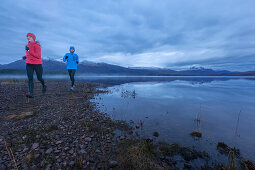 Young couple running along Loch Maree, Northwest Highlands in background, Scotland, United Kingdom