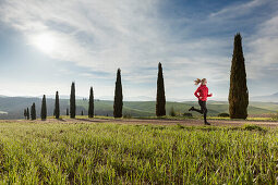 Young woman jogging along a path with cypresses, Tuscany, Italy