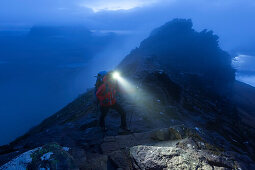 Junge Frau mit Stirnlampe steigt in der Dämmerung auf den Gipfel des Stac Pollaidh, Assynt, Schottland, Großbritannien