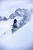 Junger Snowboarder steigt durch den Schnee in den Bergen, Pitztal, Tirol, Österreich
