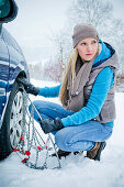 Woman applying chain to tire in snow, Styria, Austria