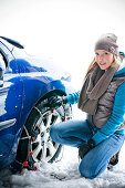 Woman applying chain to tire in snow, Styria, Austria