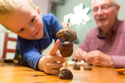 Boy (3 years) and grandfather making chestnut figures, Leipzig, Saxony, Germany