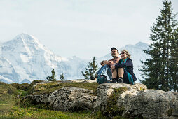 Paar rastet auf einem Felsen, Eiger, Mönch und Jungfrau im Hintergrund, Beatenberg, Berner Oberland, Kanton Bern, Schweiz