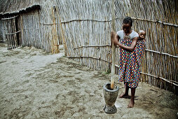 Young mother from the Lozi tribe with baby pounding grain in a big wooden mortar, Caprivi region, Namibia, Africa