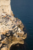 Menschen entspannen sich in einem Café an der Küste unterhalb der Stadtmauer der Altstadt, Dubrovnik, Dalmatien, Kroatien, Europa