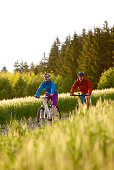 Two cyclists riding electric bicycles between fields, Tanna, Thuringia, Germany