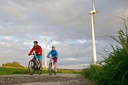 Two cyclists riding electric bicycles between fields, Tanna, Thuringia, Germany