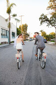 Young newlywed couple cycling along street, rear view