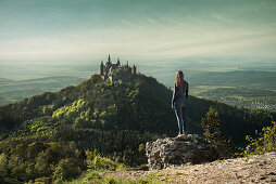 Young woman looking towards Hohenzollern castle from Zeller mountain, Hechingen Bissingen, Swabian Alp, Baden-Wuerttemberg, Germany