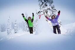 Children cheering beside a snowman, Passo Monte Croce di Comelico, South Tyrol, Italy