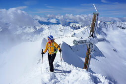 Female back-country skier beside summit cross at Grosser Moeseler, Zillertal Alps, South Tyrol, Italy