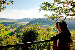 A couple enjoying the view across the Eder valley to Schmittlotheim from the Hagenstein viewpoint in Kellerwald-Edersee National Park, Schmittlotheim, Hesse, Germany, Europe