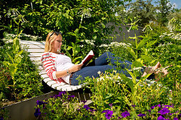 Eine junge blonde Frau liegt auf einer Bank im Kurpark Bad Wildungen und liest ein Buch, Bad Wildungen, Nordhessen, Hessen, Deutschland, Europa