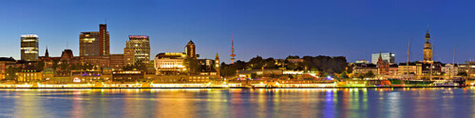 Panorama of Hamburg with view over the river Elbe to illuminated St. Pauli-Landungsbruecken with skyscrapers, Pegelturm, Heinrich-Hertz-Turm, Telemichel, museum ship Rickmer Rickmers, churches St. Michaelis, Nicolai and Katharinen, Hanseatic Trade Center,