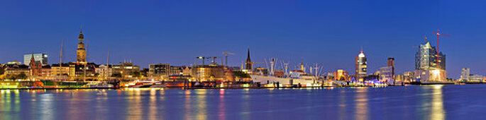 Panorama of Hamburg with view over the river Elbe to illuminated St. Pauli-Landungsbruecken with Pegelturm, Heinrich-Hertz-Turm, Telemichel, museum ship Rickmer Rickmers, churches St. Michaelis, Nicolai and Katharinen, Hamburg, Germany