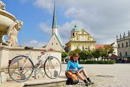 Cyclist resting at Marienbrunnen fountain, Kapellplatz, Altoetting, Upper Bavaria, Germany