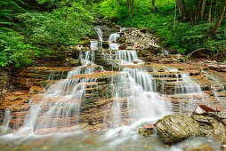 Waterfall cascading down over red rocks, Taugl, Salzkammergut, Salzburg, Austria