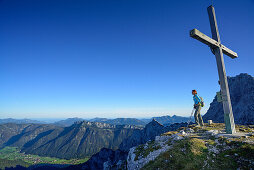 Woman reaching the summit cross on Ulrichshorn while hiking, Nurracher Hoehenweg, Ulrichshorn, Loferer Steinberge range, Tyrol, Austria