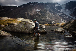 Man wading through a mountain lake, near Bremer Hütte (ca. 2413 m), rear of Gschnitz Valley, Stubai Alps, Tyrol, Austria
