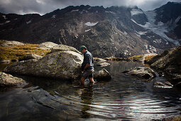 Mann durch einen Bergsee watend, an der Bremer Hütte (ca. 2413 m), Hinteres Gschnitztal, Stubaier Alpen, Tirol, Österreich