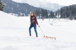 Young woman pulling a sled, Spitzingsee, Upper Bavaria, Germany