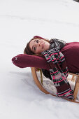 Junge Frau liegt auf einem Schlitten, Spitzingsee, Oberbayern, Bayern, Deutschland