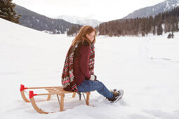 Junge Frau sitzt auf einem Schlitten, Spitzingsee, Oberbayern, Bayern, Deutschland
