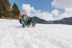 Zwei junge Frauen rodeln bergab, Spitzingsee, Oberbayern, Bayern, Deutschland