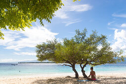 Frau sitzt unter einem niedrigen Baum am Strand, Gili Meno, Lombok, Indonesien
